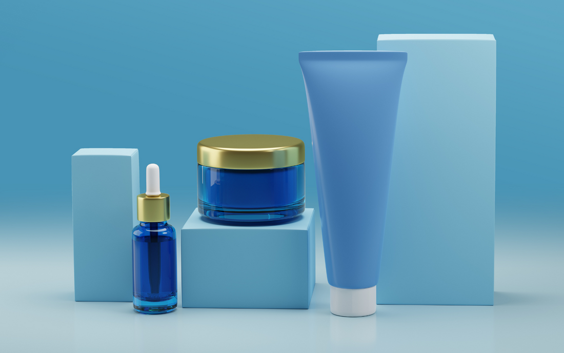 Indigo private label cosmetics set with serum dropper, cream jar, and tube packaging on a blue background.