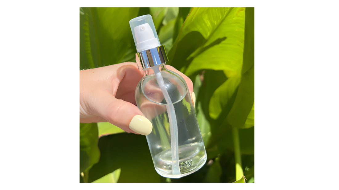  Indigo Private Label toner in a clear glass mist spray bottle for skincare held against green foliage.