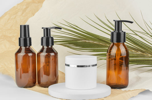 Cosmetic bottles with dispensers and a white jar of moisturizer with palm leaves in the background. 