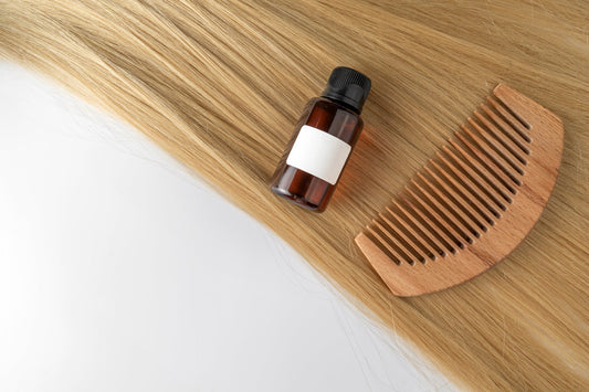 Amber dropper bottle and wooden comb placed on long blonde hair strands.