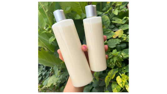 Hand holding two hair growth shampoo bottles in fresh greenery, part of Indigo Private Label's haircare line.