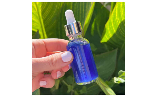 Hand holding a copper peptide dropper bottle against green leaves by Indigo Private Label. 