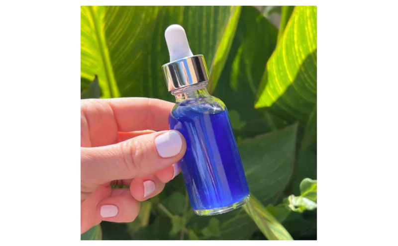 Hand holding a copper peptide dropper bottle against green leaves by Indigo Private Label. 