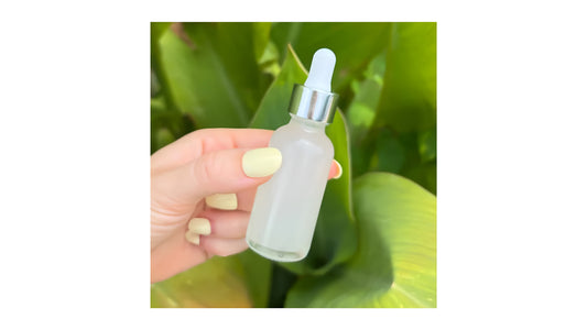 Hyaluronic acid dropper bottle from Indigo Private Label, held against lush green leaves.