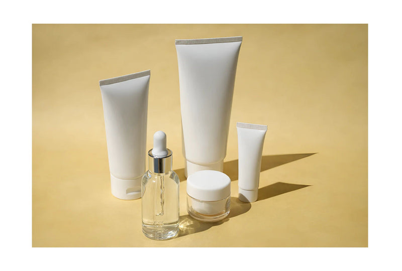  Indigo Private Label Makeup sample kit with tubes, dropper bottle, and jar against a yellow backdrop. 