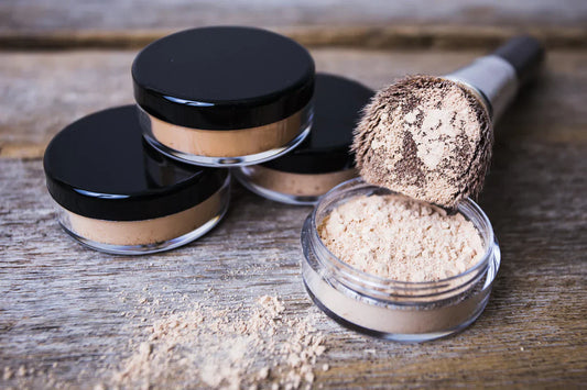 Indigo Private Label loose mineral powder jars with a makeup brush on a rustic wood surface.