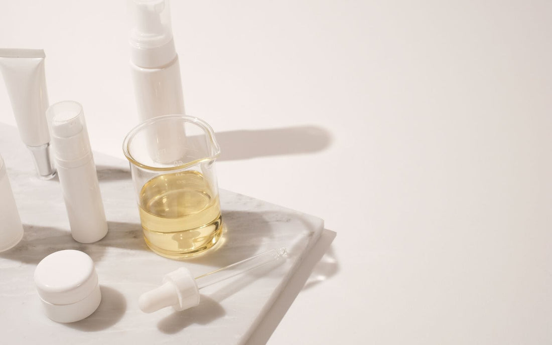 Indigo Private Label skincare containers and oil beaker displayed on a marble surface.