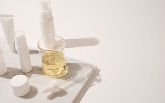 Indigo haircare bottles and serum dropper arranged with cosmetic ingredients on a marble tray.