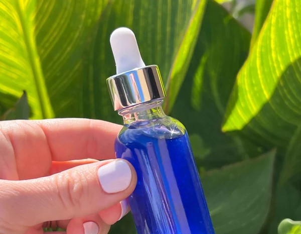 A hand holding a sleek bottle of peptide serum with a dropper applicator by Indigo Private Label. 