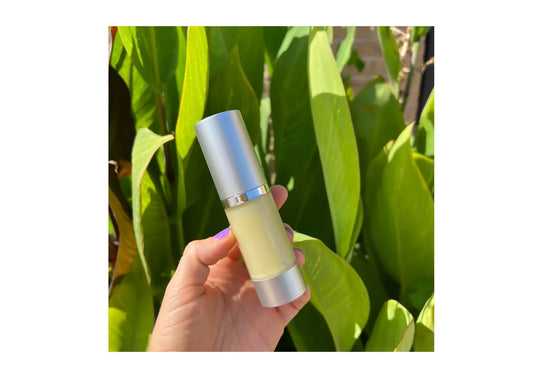 Hand holding an Indigo Private Label skincare bottle outdoors against lush green leaves.