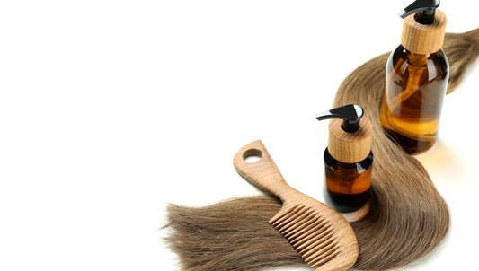 Amber pump bottles with wooden caps beside a wooden comb and brown hair strands on a white surface.