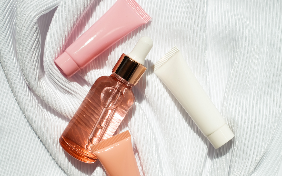 Indigo Private Label serum dropper bottle and three skincare tubes on white textured fabric.