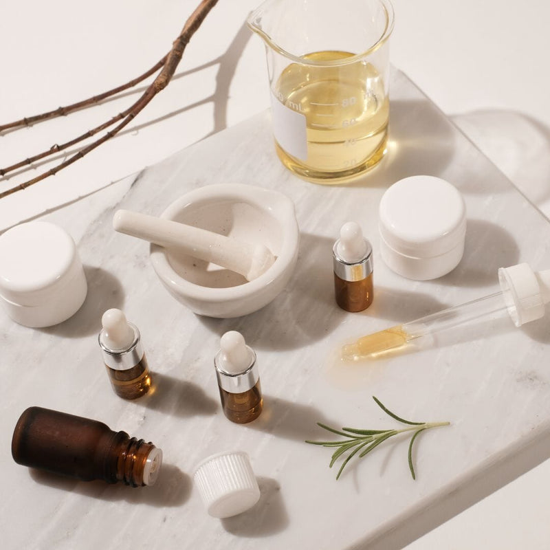 Indigo Private Label skincare oils and jars arranged with lab tools on a clean marble surface.